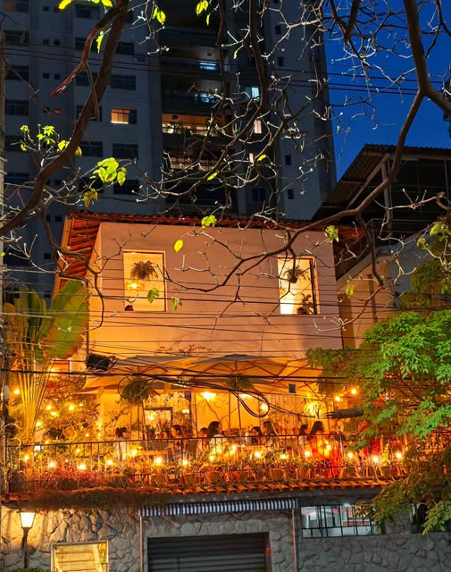 Fachada da casa à noite, com a varanda iluminada por luzinhas e as janelas acesas.